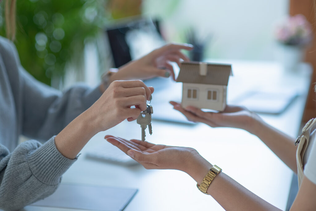 Midsection Of Real Estate Agent Giving House Key To Customer While Sitting In Office