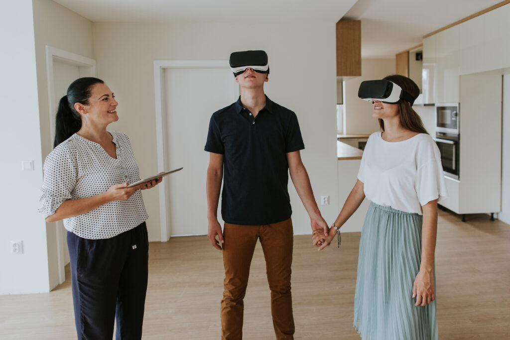 Young man and woman holding hands and wearing virtual reality headsets on house viewing with estate agent.