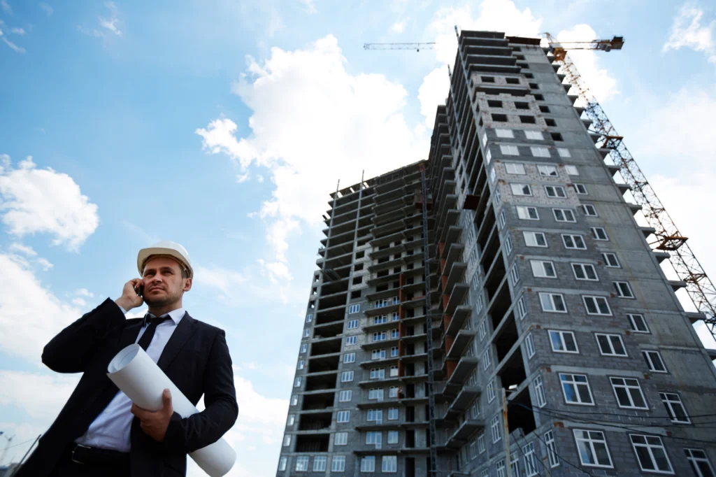 Elegant investor in helmet talking on mobile phone by unfinished building
