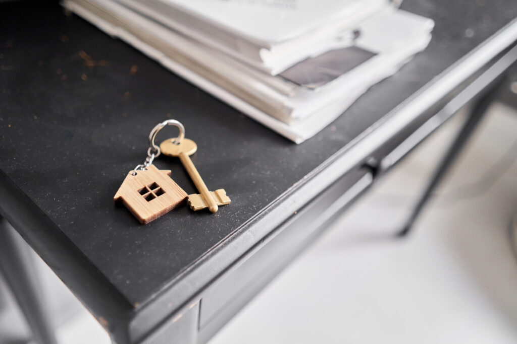 Key with house shaped keychain on dust table . Modern light apartment interior. Mortgage concept. Real estate, moving home or relating property.. High quality photo