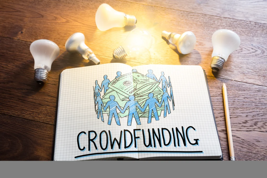 Crowdfunding Concept In Notepad Near Glowing Lightbulbs