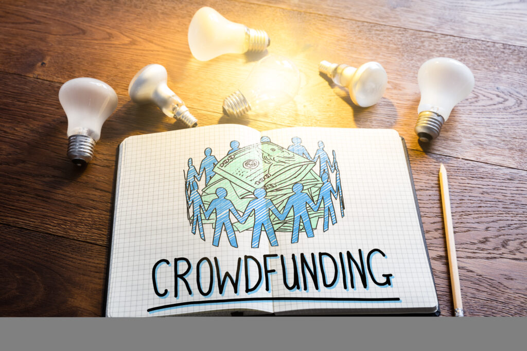 Crowdfunding Concept In Notepad Near Glowing Lightbulbs