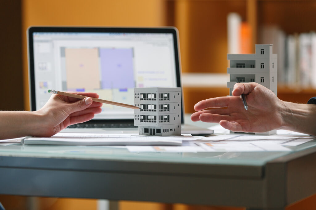 Architects discussing model of a house in a studio with blueprints and laptop on a table. Architectural desigh bureau working concept