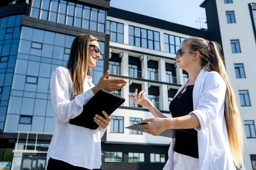 Two businesswoman holding tablets and talking opposite office building