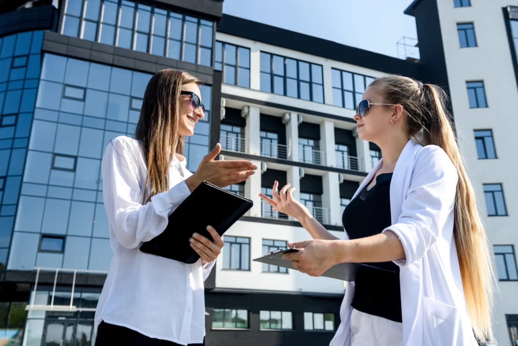 Two businesswoman holding tablets and talking opposite office building